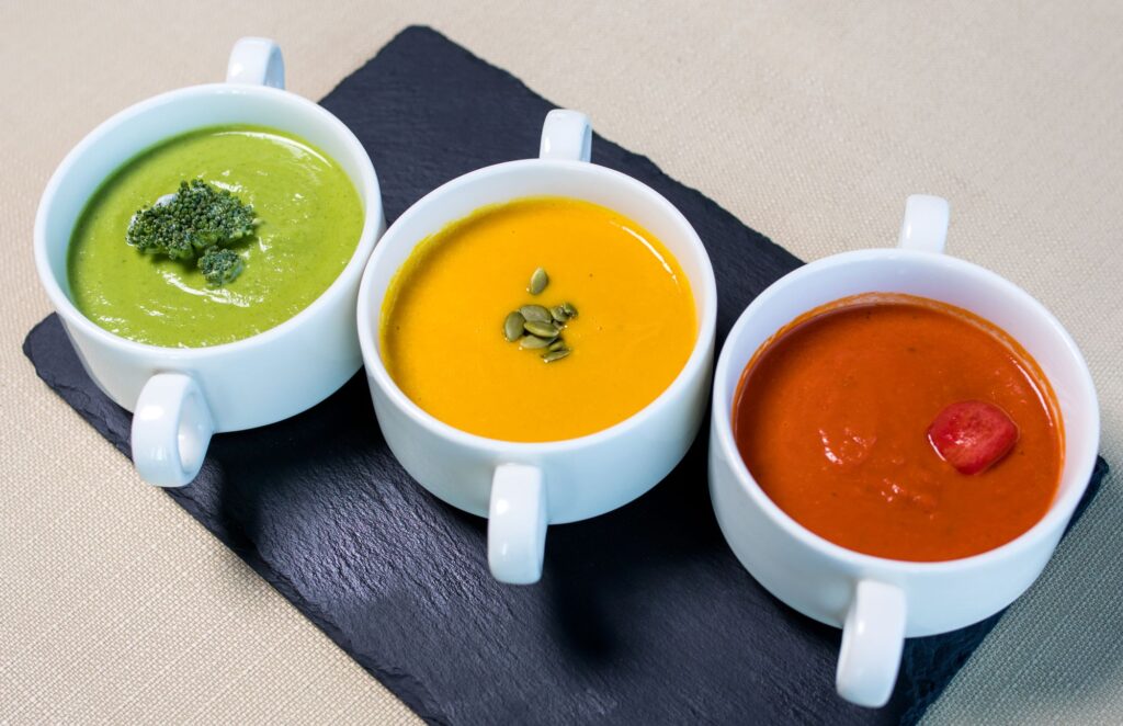 Three bowls of blended vegetable soup: broccoli, pumpkin and tomato