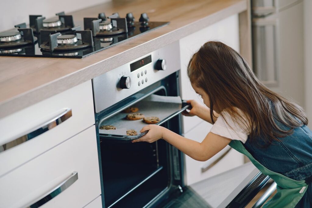 A young girl places a tray of cookies in the oven in a contemporary kitchen setting