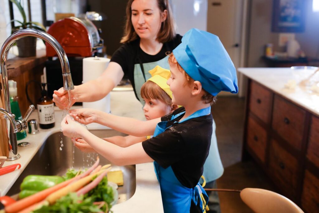 Mother and children wearing chef hats washing hands while preparing food together in the kitchen
