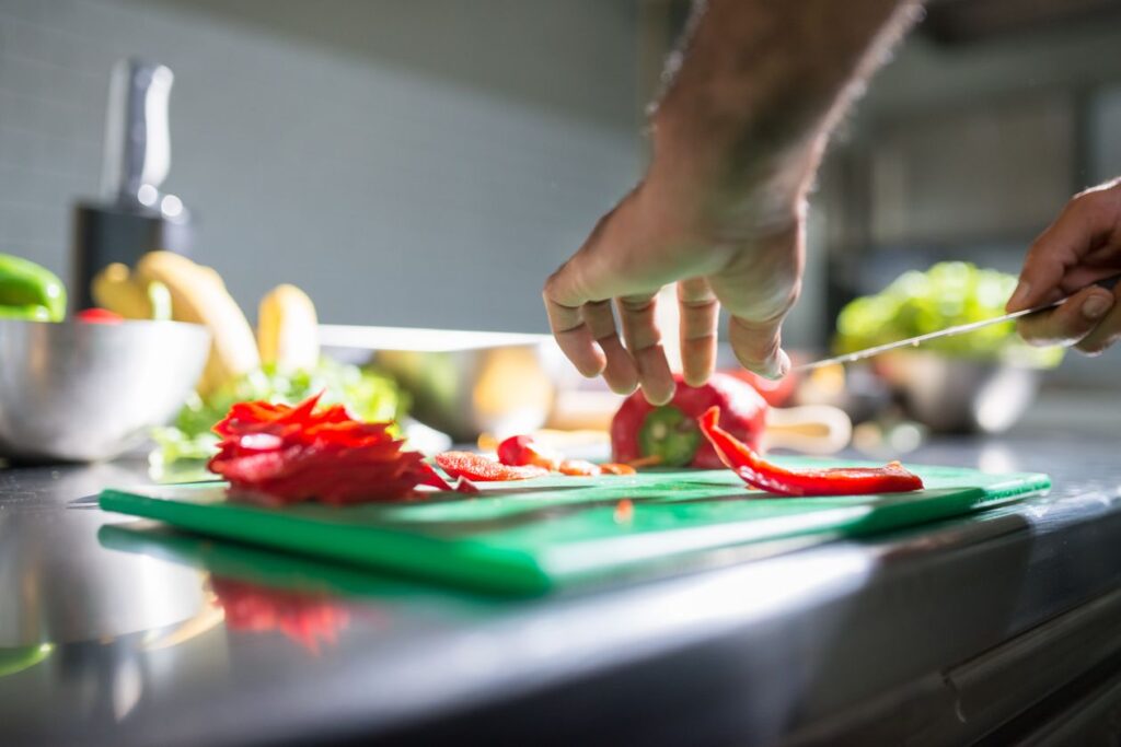Hands slicing red bell pepper on a chopping board in a kitchen setting, ideal for culinary visuals
