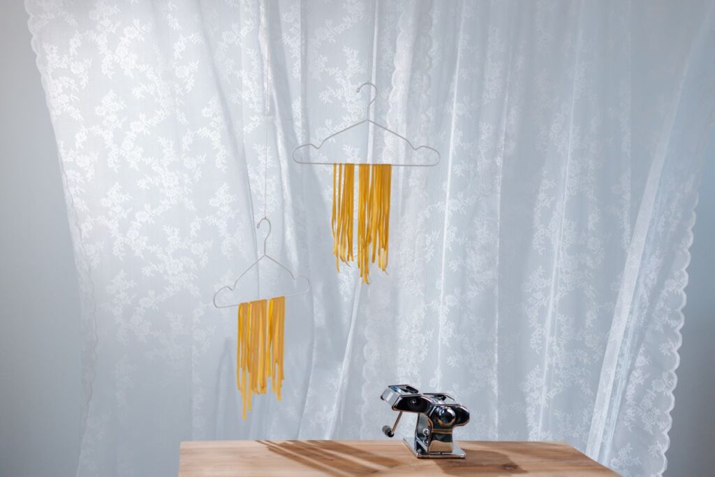Fresh pasta hanging to dry beside a hand-crank pasta machine