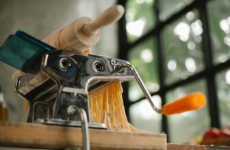 Stainless steel pasta maker cutting fresh pasta on a wooden table
